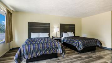 A hotel room with two beds, a nightstand, a lamp, and a window with curtains.