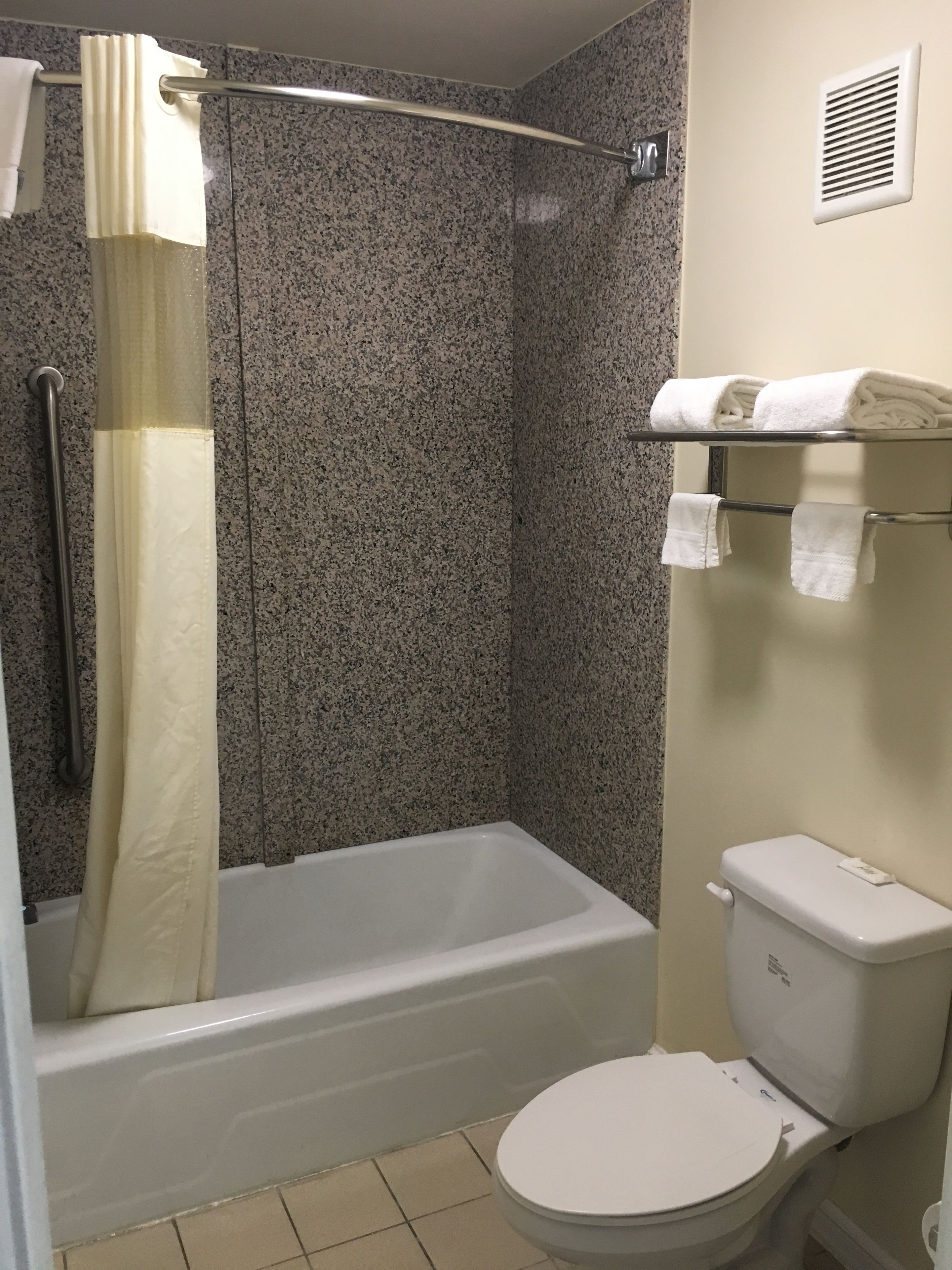 A bathroom with a bathtub, shower curtain, toilet, and towel rack.