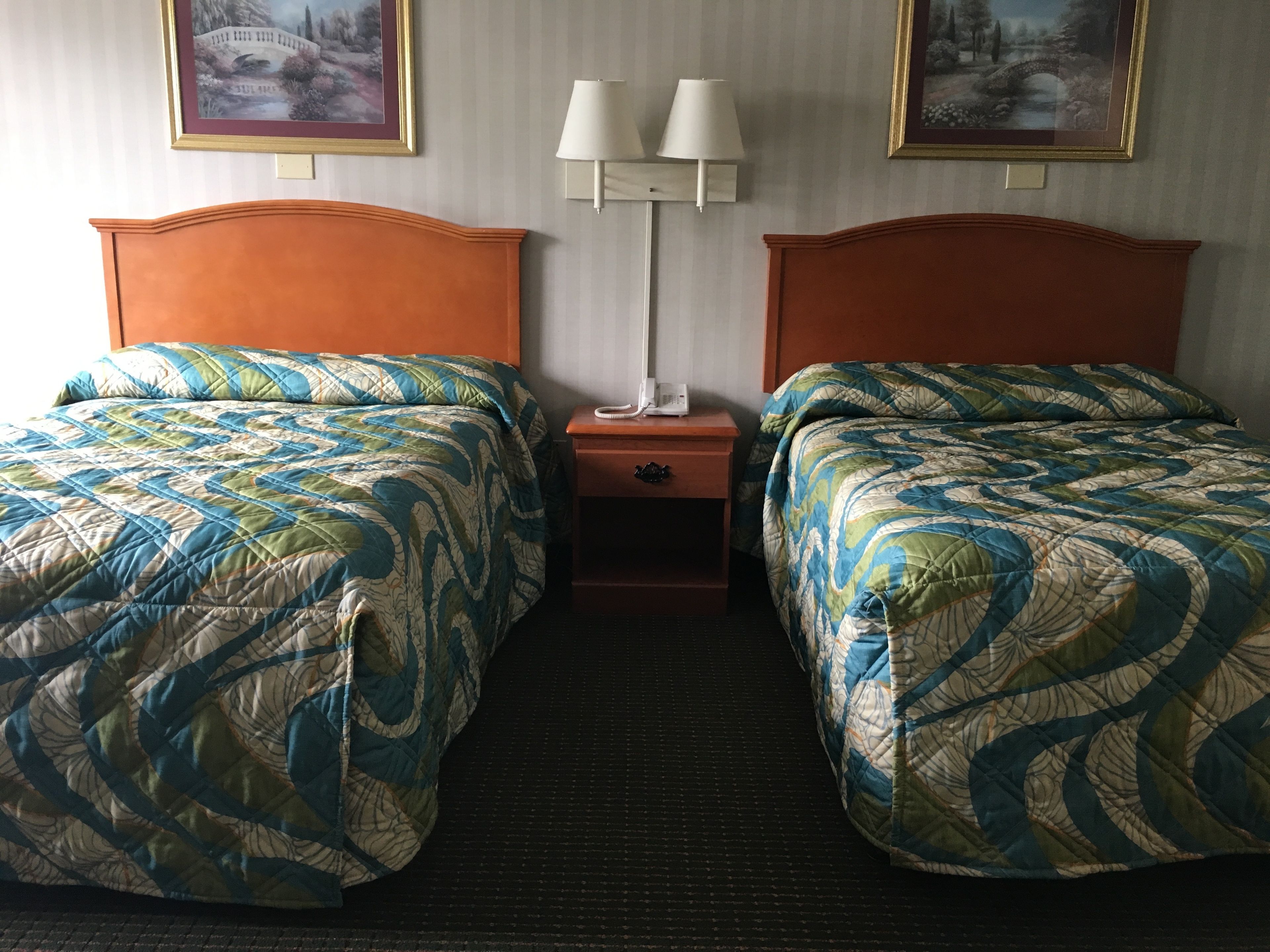 A hotel room with two beds, each with a patterned quilt, a nightstand with a lamp, and framed pictures on the wall.