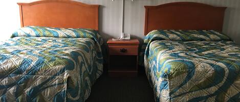A hotel room with two beds, each with a patterned quilt, a nightstand with a lamp, and framed pictures on the wall.