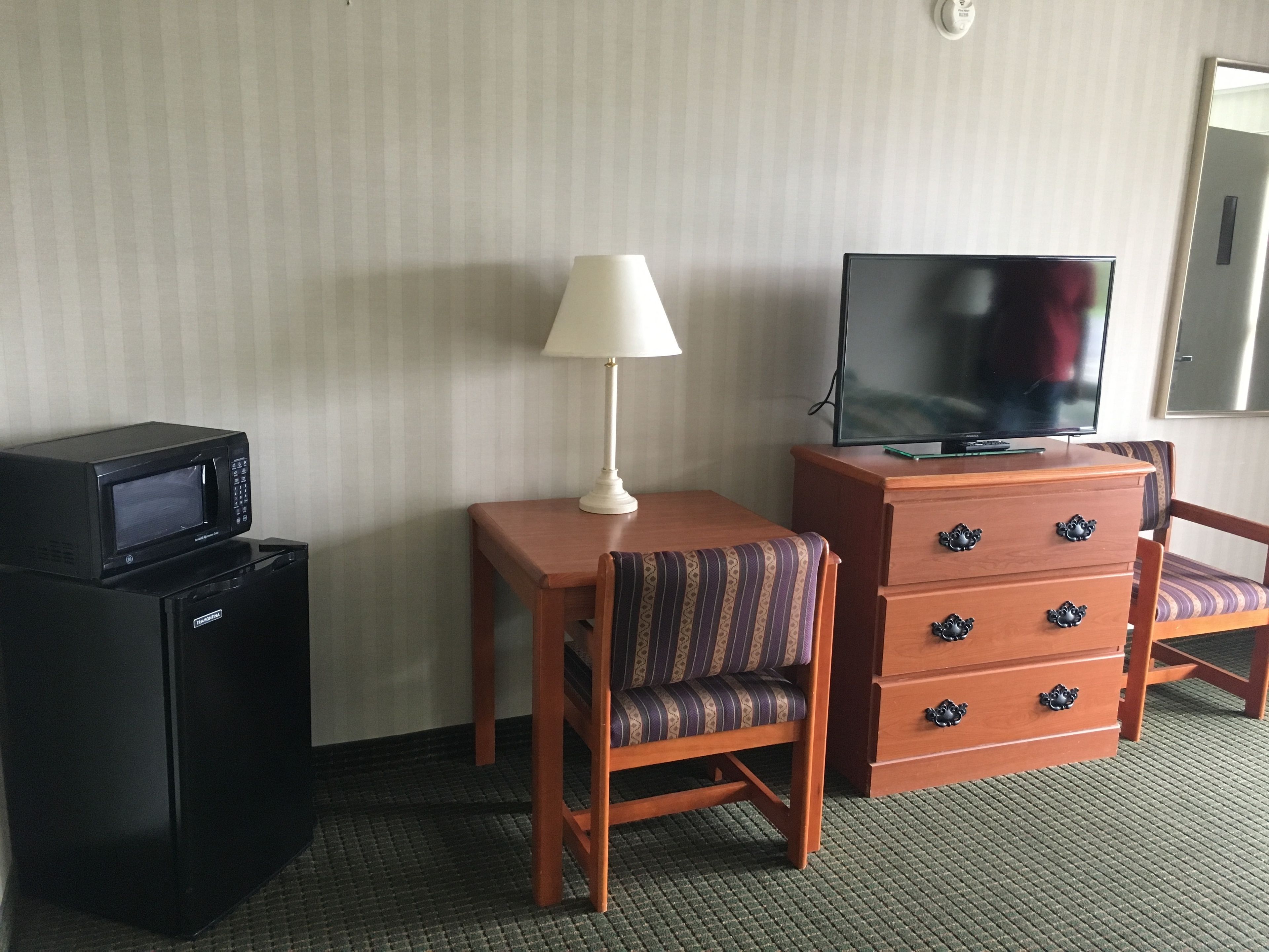 A hotel room with a desk, a chair, a television, a lamp, and a microwave.