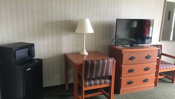 A hotel room with a desk, a chair, a television, a lamp, and a microwave.