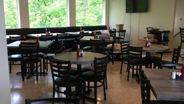 A spacious dining area with multiple tables and chairs, large windows offering a view of greenery, and a flat-screen TV mounted on the wall. - The North Star Inn (Corinth)
