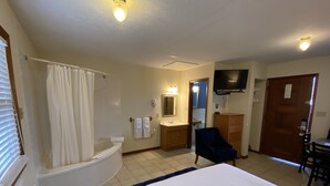 A hotel room with a bathtub, a sink, a mirror, a television, a chair, and a desk. - The North Star Inn (Corinth)