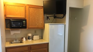 A compact kitchen with wooden cabinets, a microwave, a refrigerator, a coffee maker, and a toaster. - The North Star Inn (Corinth)