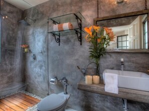 Ein modernes Badezimmer mit Marmorwand, einer Glasablage mit Handtüchern, Holzboden, Toilette, Waschbecken und Spiegel.