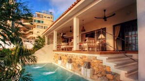 A pool area with a stone wall, a staircase, and a balcony with outdoor furniture. - Villas Enrique (Puerto Vallarta)