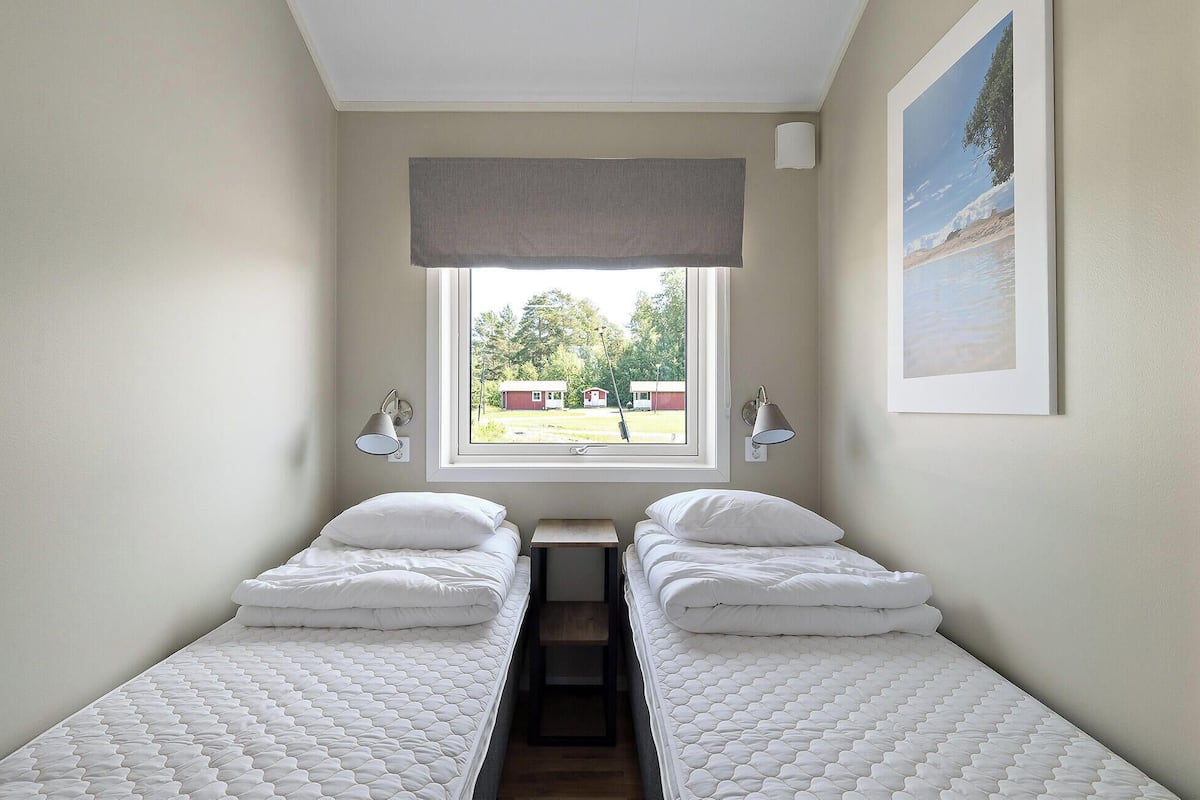 Una habitación con dos camas individuales, una ventana con vista a edificios y un cuadro en la pared.