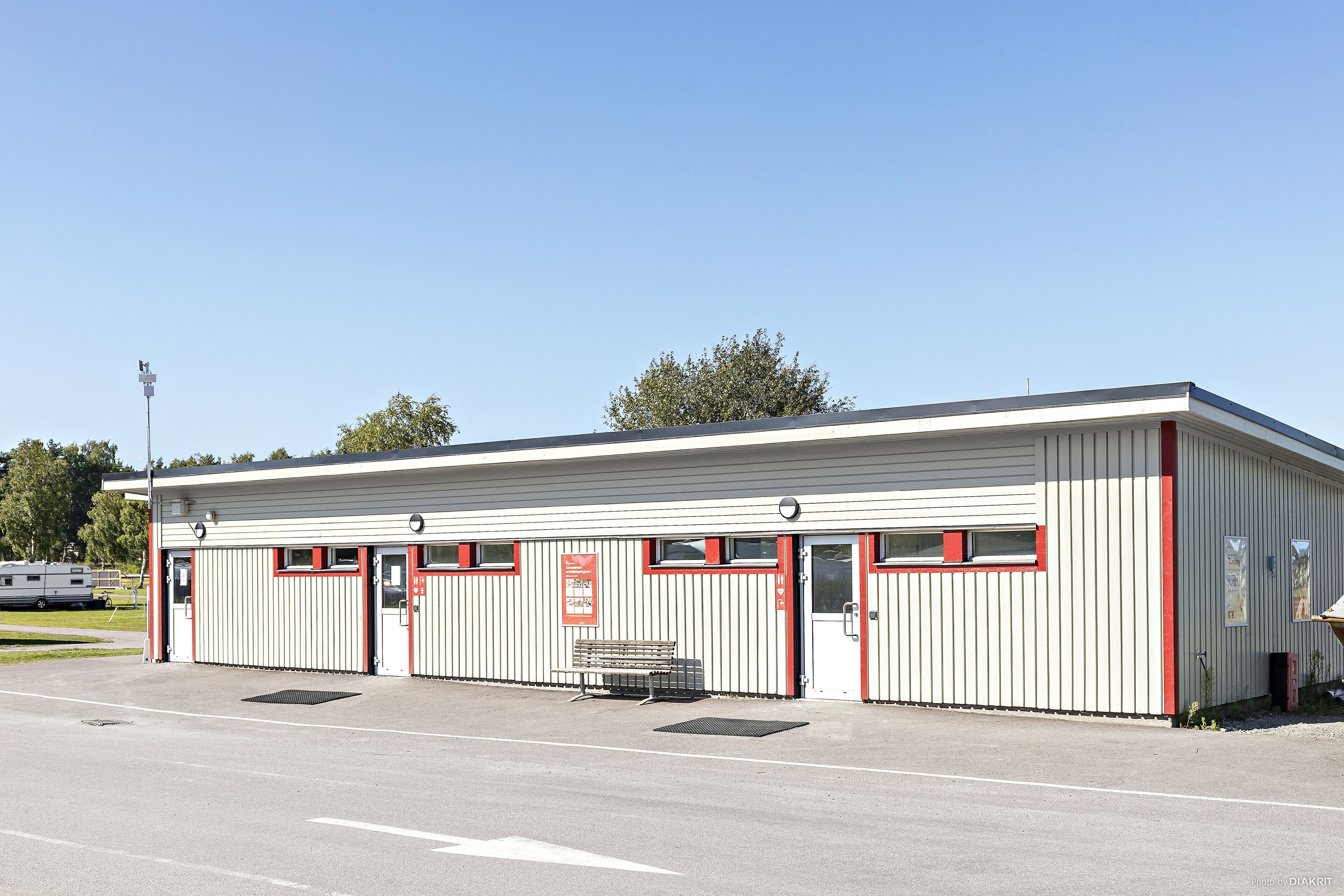 A single-story building with a flat roof, a red door, and a bench in front.
