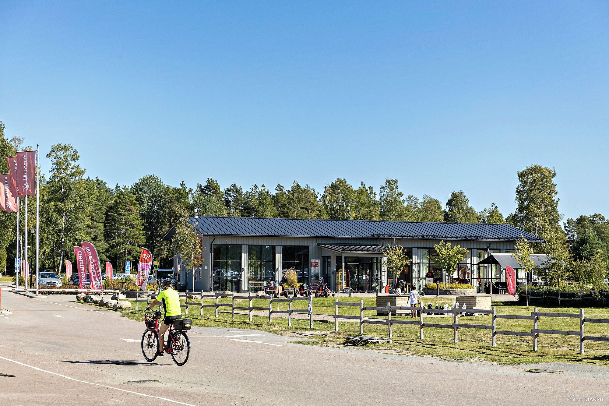 A building with a covered outdoor area, a bicycle path, and a fenced grassy area.