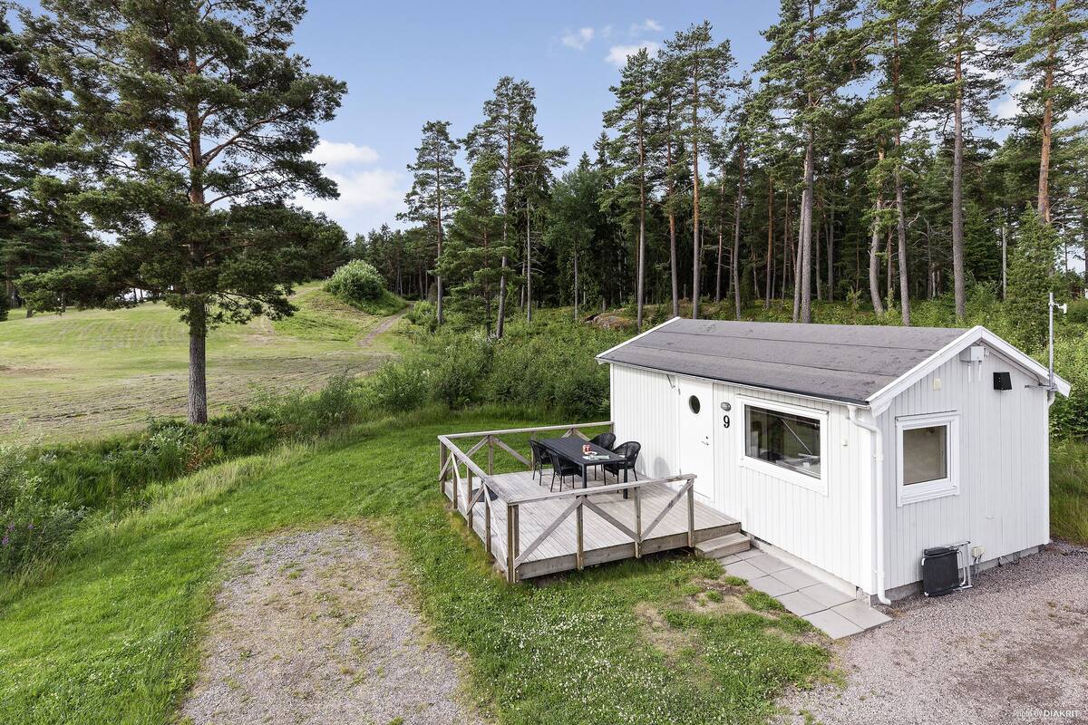 Una cabaña pequeña con terraza y zona de estar exterior, rodeada de un paisaje boscoso.