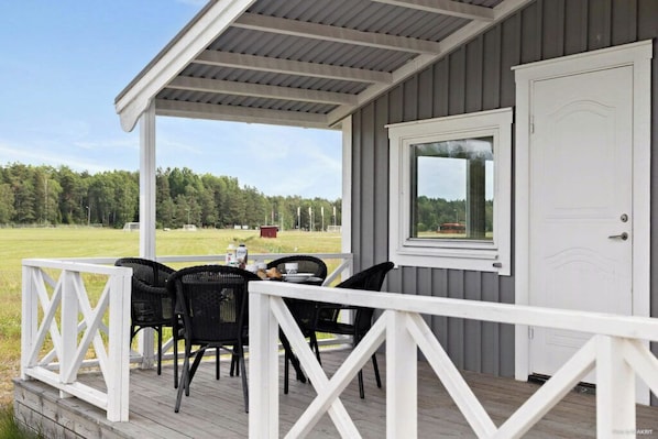 A covered outdoor seating area with a table and chairs, a white door, and a view of a grassy field. - First Camp Karlstad (Karlstad)