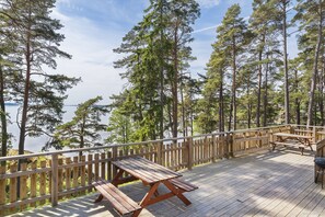 A wooden deck with picnic tables overlooking a lake, surrounded by tall trees. - First Camp Kolmården (Kolmården)