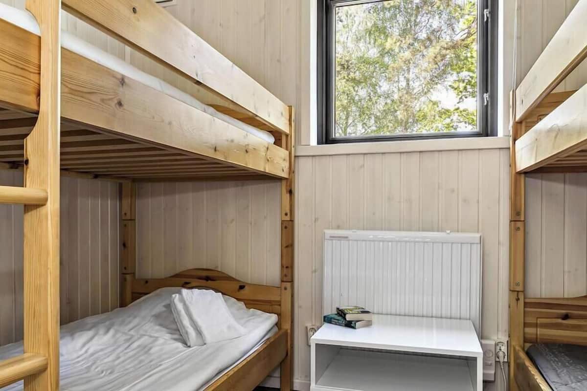 Een slaapkamer met een stapelbed, een raam, een radiator en een klein plankje met boeken.