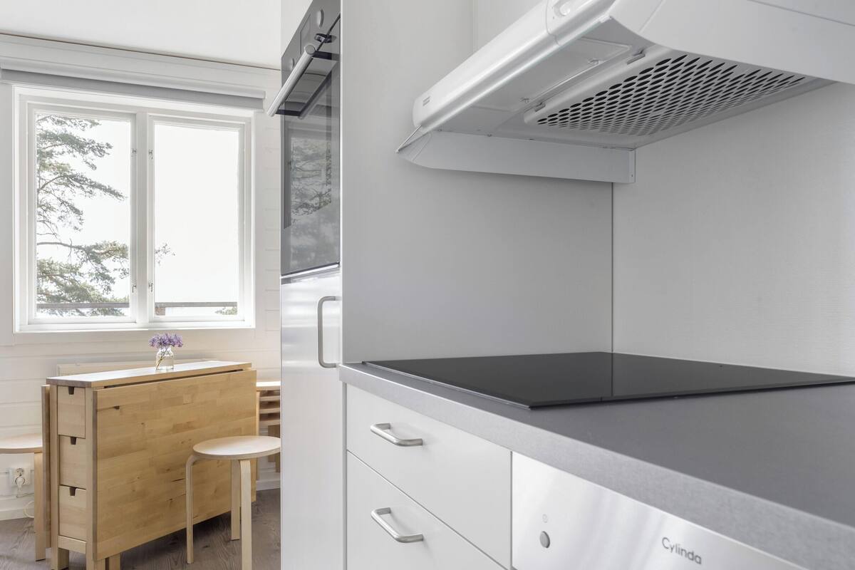 Een moderne keuken met een houten tafel, een zwart aanrecht en een raam met uitzicht op bomen.