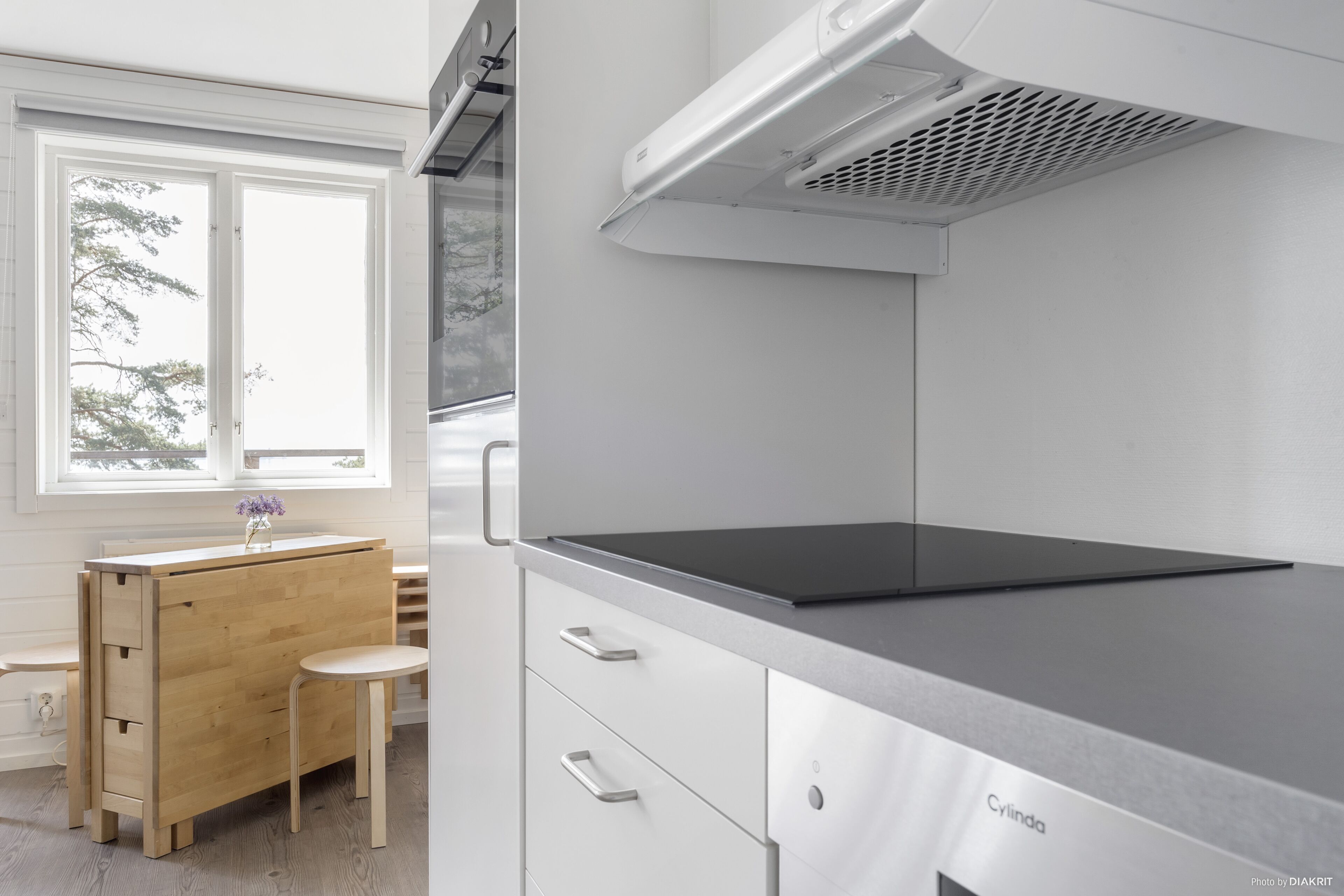 A modern kitchen with a wooden cabinet, a small stool, and a stainless steel countertop.