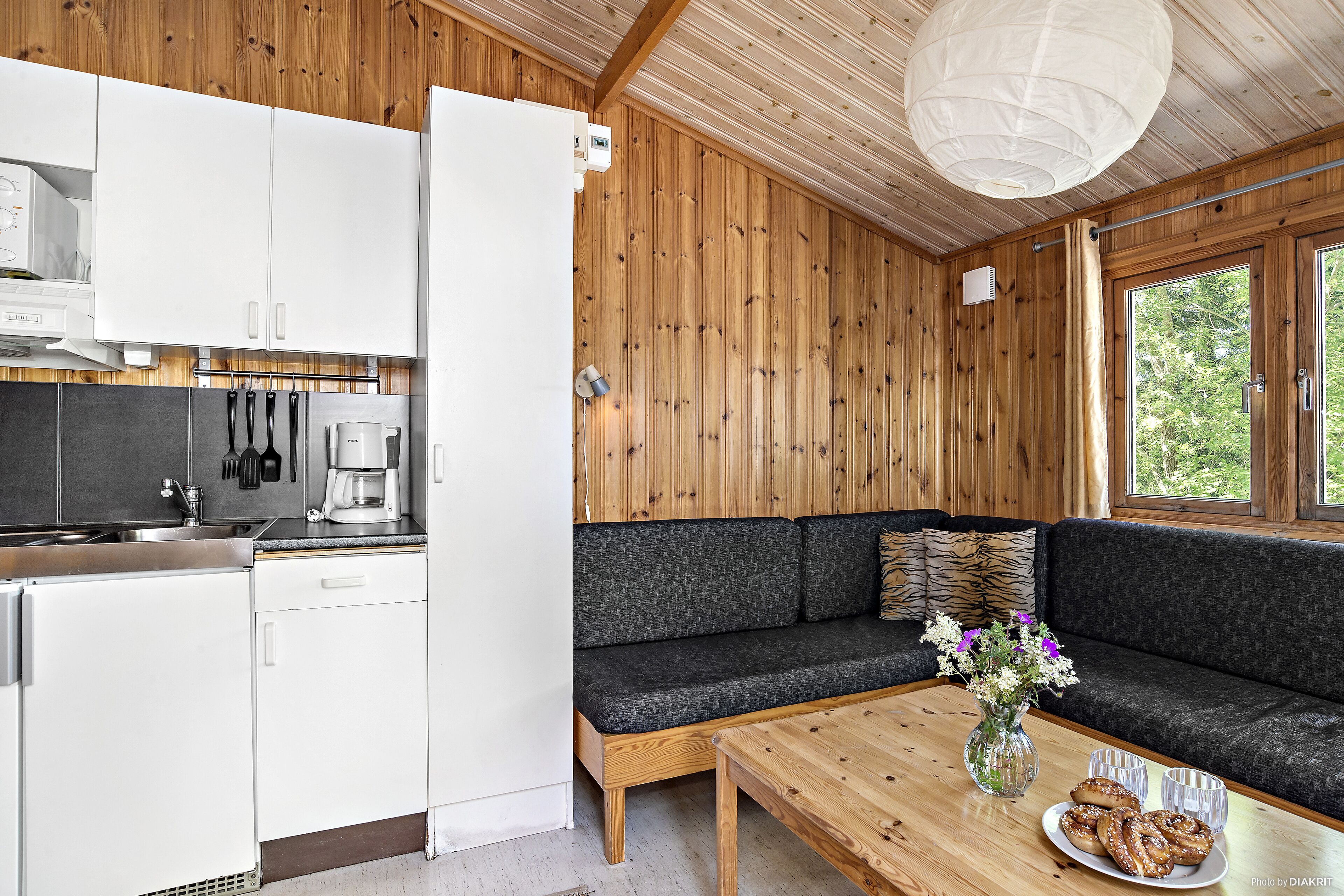 A modern kitchen with white cabinets, a coffee machine, and a wooden dining table with a vase of flowers.