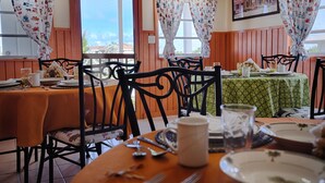 A dining area with wooden tables and chairs, a green tablecloth, and a view of the outdoors. - Chesters Bonefish Lodge (Chesters)