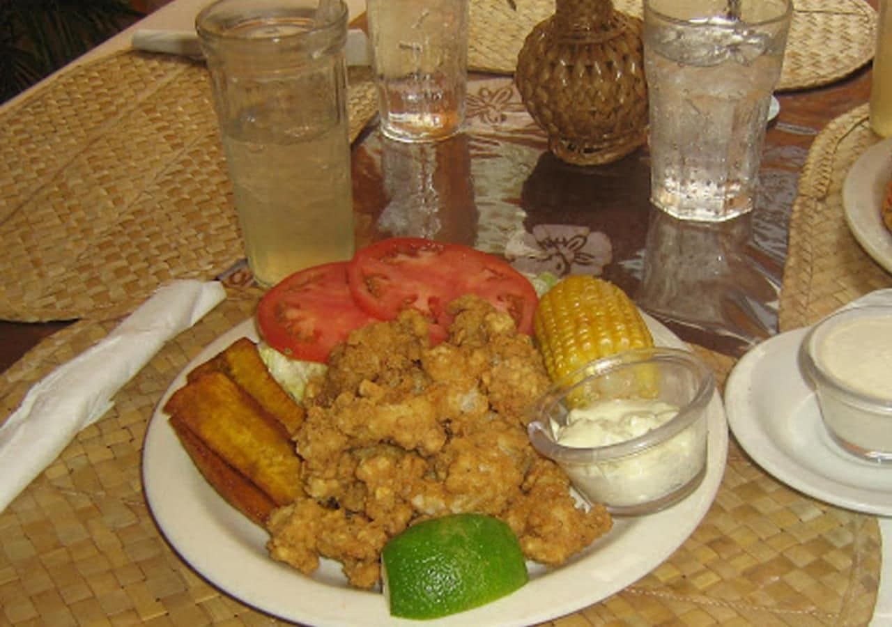 Un plato de comida con pollo frito, maíz y una cuña de lima.