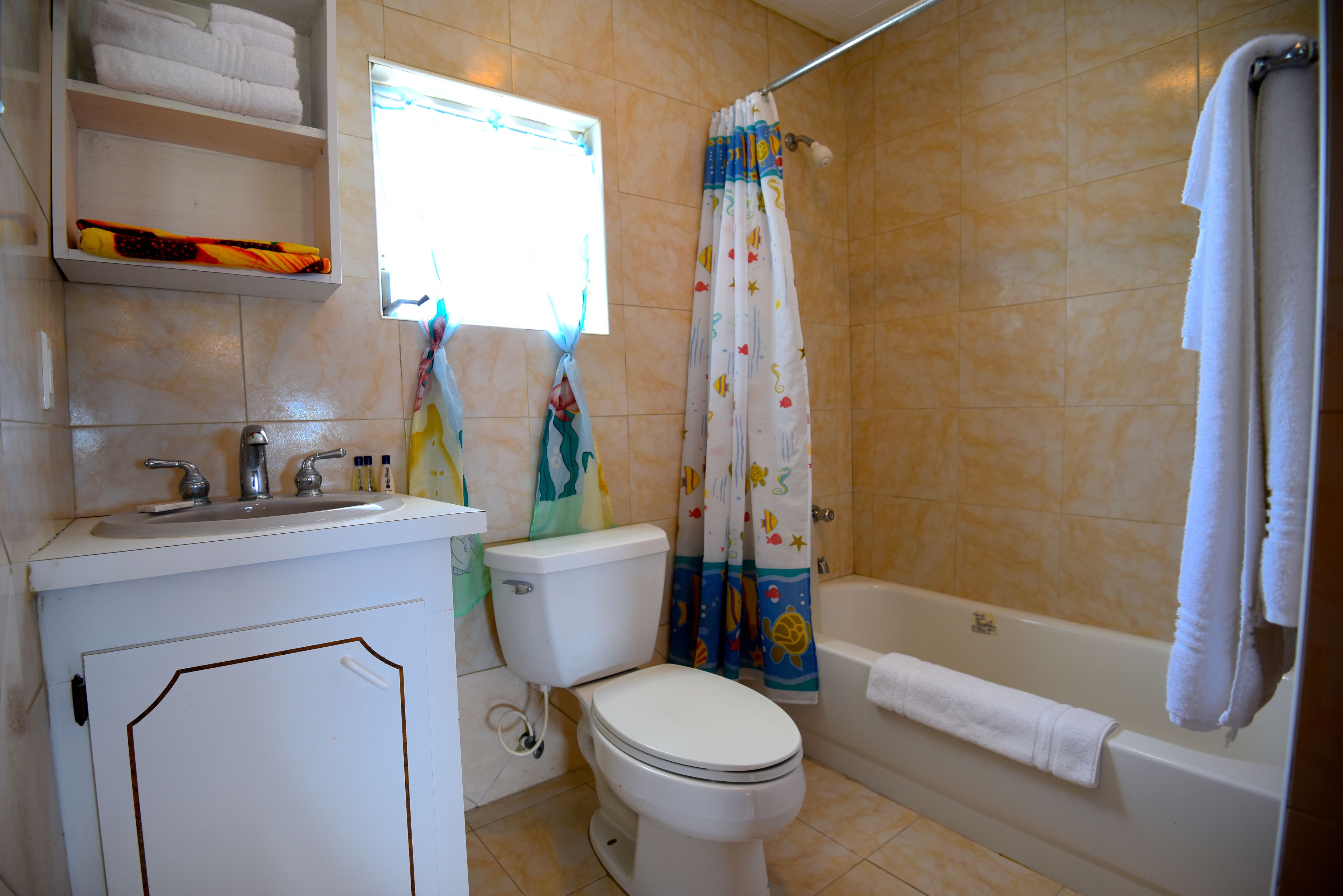 Une salle de bain équipée de toilettes, d’un lavabo et d’une baignoire. On y trouve des serviettes et un rideau de douche.