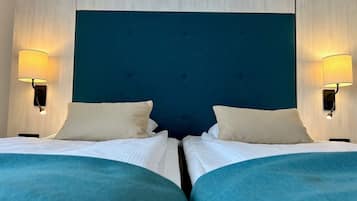 Habitación de hotel con dos camas, cada una con cabecero azul y ropa de cama blanca. Hay dos lámparas fijadas a la pared a cada lado de las camas.