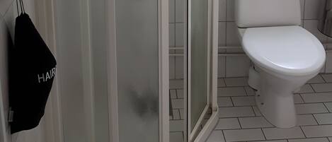 A bathroom with a white tiled floor, a white toilet, a glass shower enclosure, and a window above the toilet.