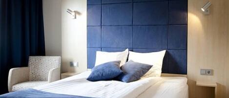 Una habitación de hotel moderna con una cama grande, un cabecero de diseño acolchado, una mesita de noche y una silla.