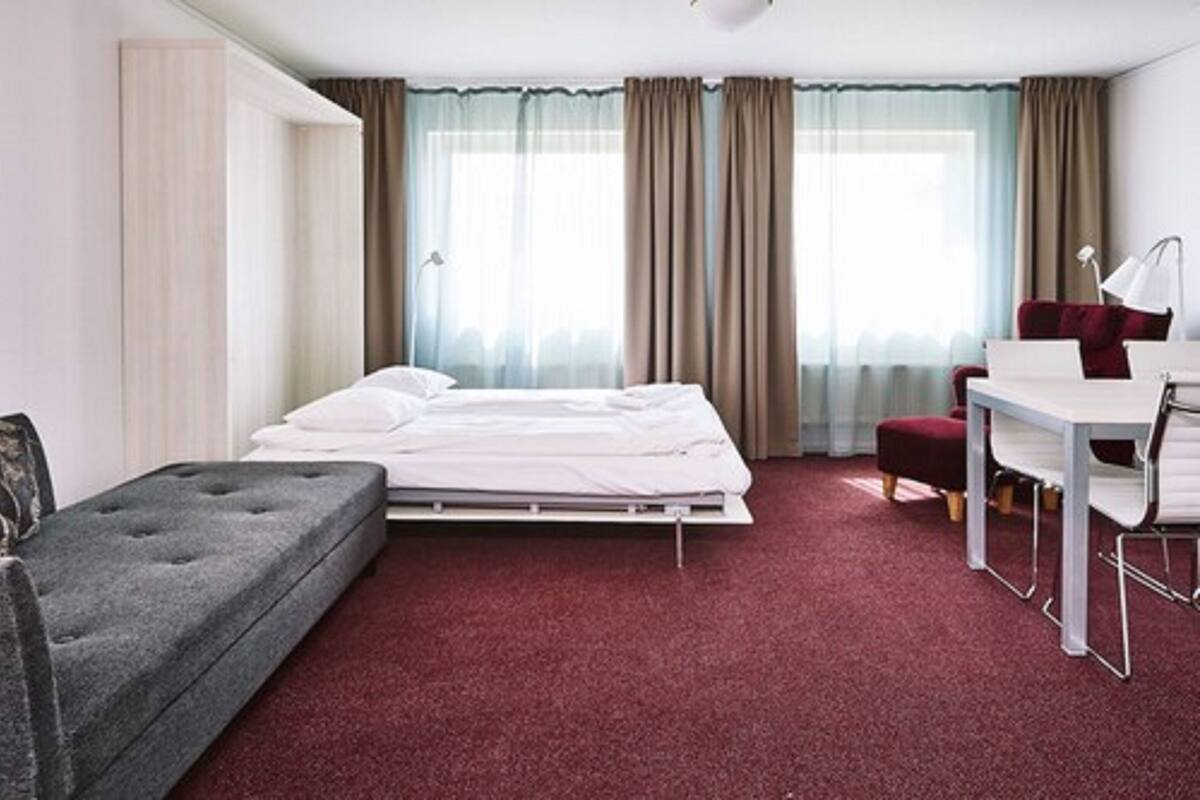 A hotel room with a bed, a desk, a chair, and a sofa.
