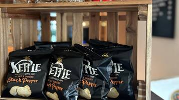 A wooden shelf with snacks and drinks, including Pringles cans and Kettle potato chips.