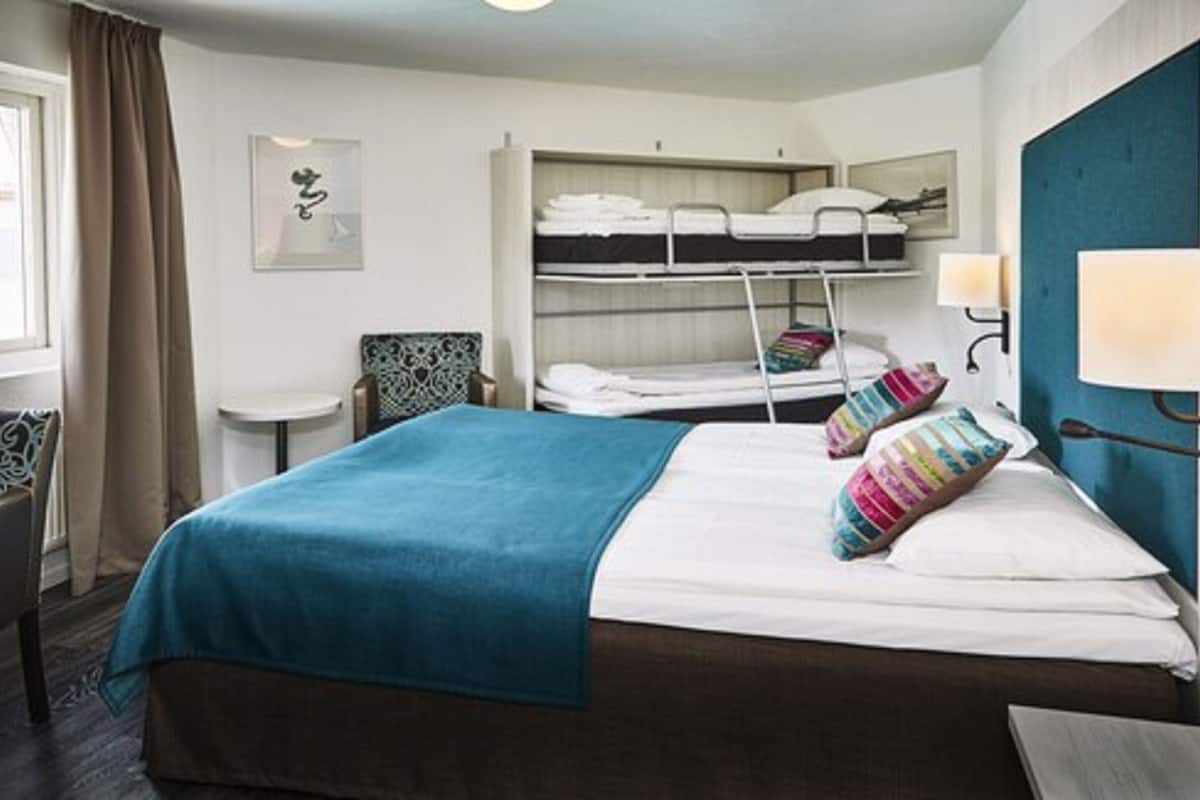 A hotel room with a single bed, a bunk bed, a small table, and a chair.