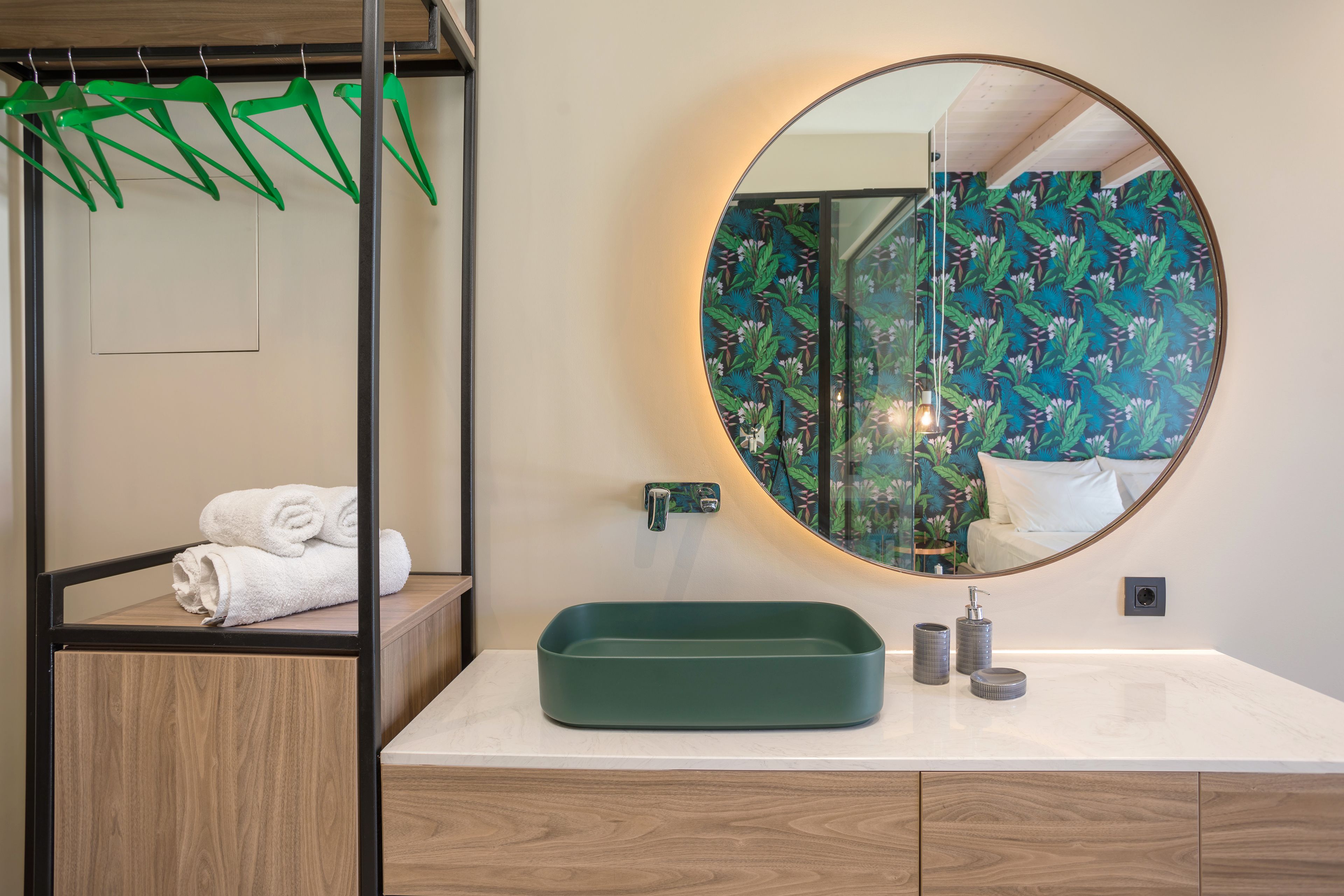 Een badkamer met een houten wastafelmeubel, een ronde spiegel en een groene wastafel.