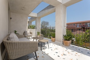 Relax on the balcony with a comfortable sofa, small table, and two chairs, surrounded by lush potted plants.