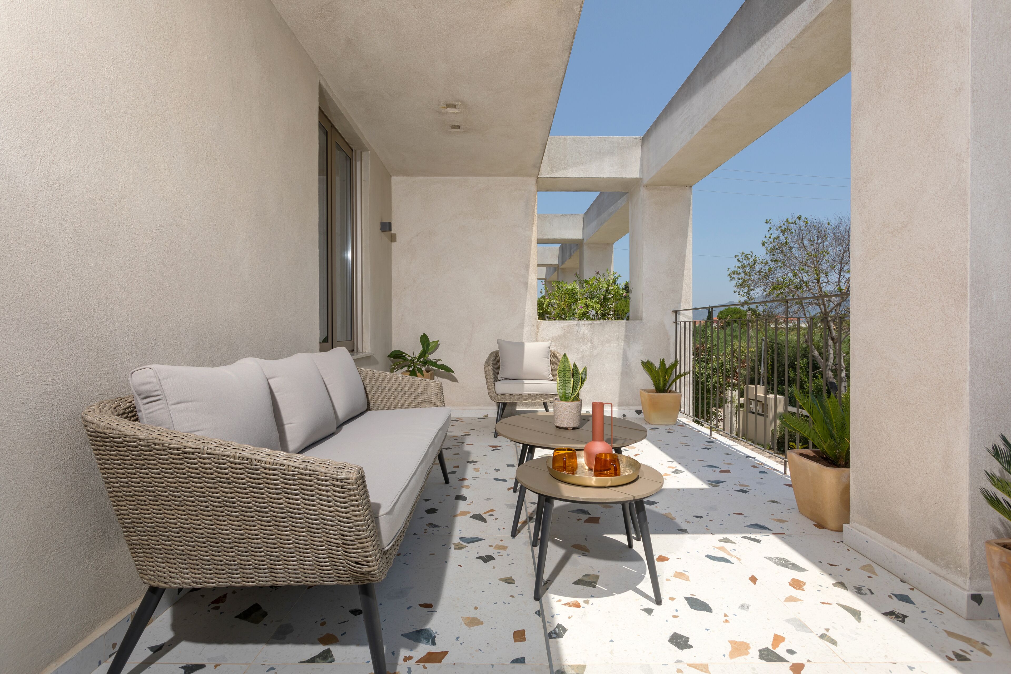 A balcony with a sofa, chairs, a small table, and potted plants.