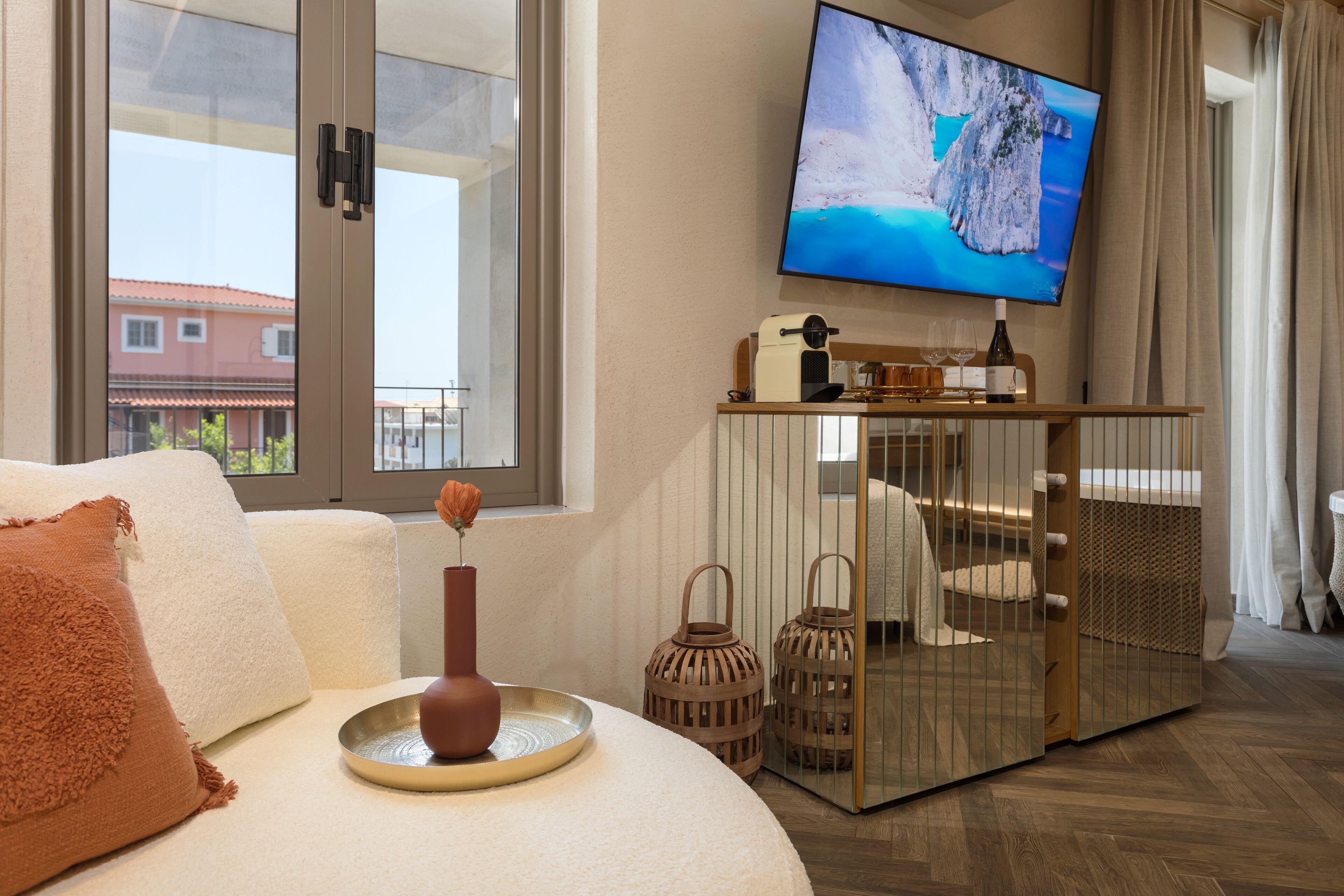 Ein modernes Hotelzimmer mit großem Fernseher, einer gemütlichen Couch, einem Tablett mit einer Vase und Blick auf ein Gebäude.