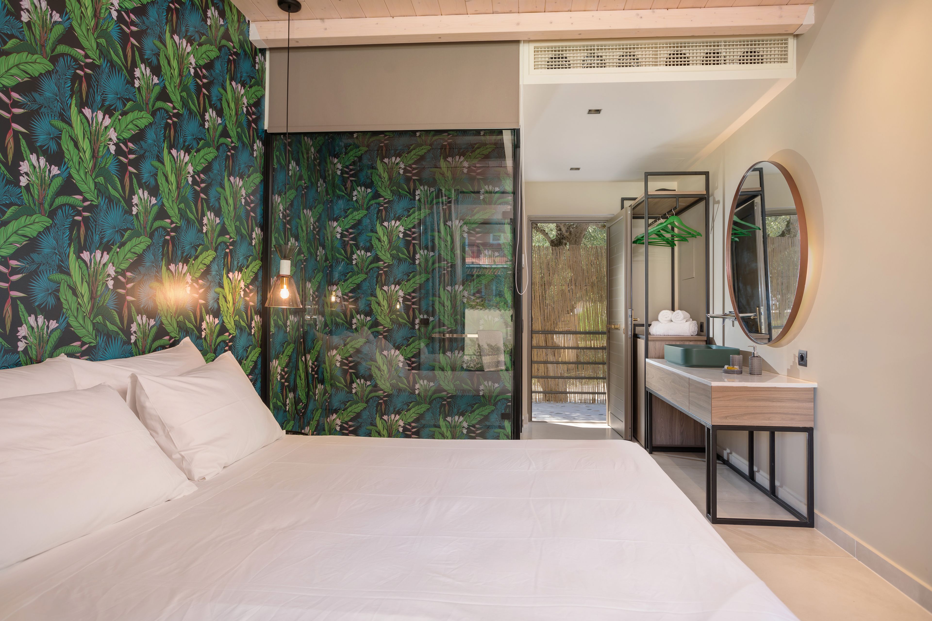 Un dormitorio moderno con una cama grande, una mesita de noche de madera, un espejo y un baño con lavamanos y toallero.