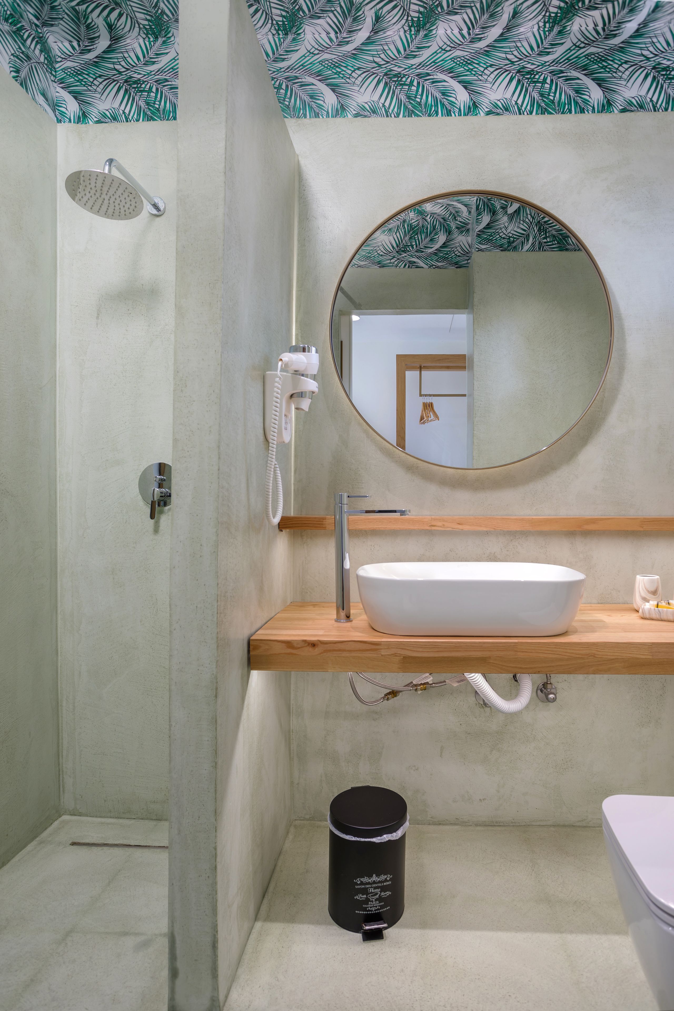A bathroom with a wooden vanity, a round mirror, a white sink, a toilet, and a shower with a handheld showerhead.