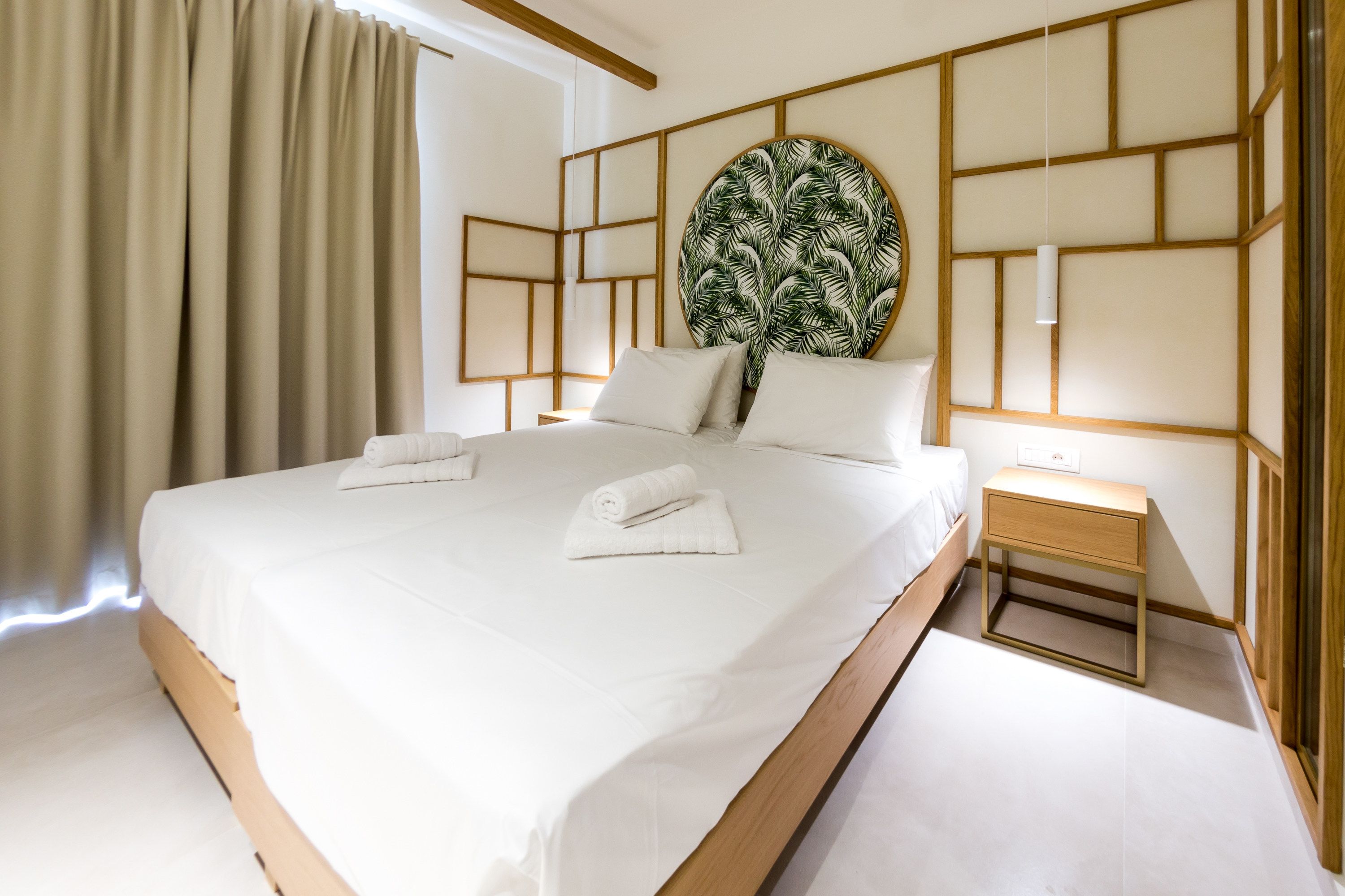 Habitación de hotel moderna con una cama grande, cabecera de madera, mesita de noche y una lámpara fijada a la pared.