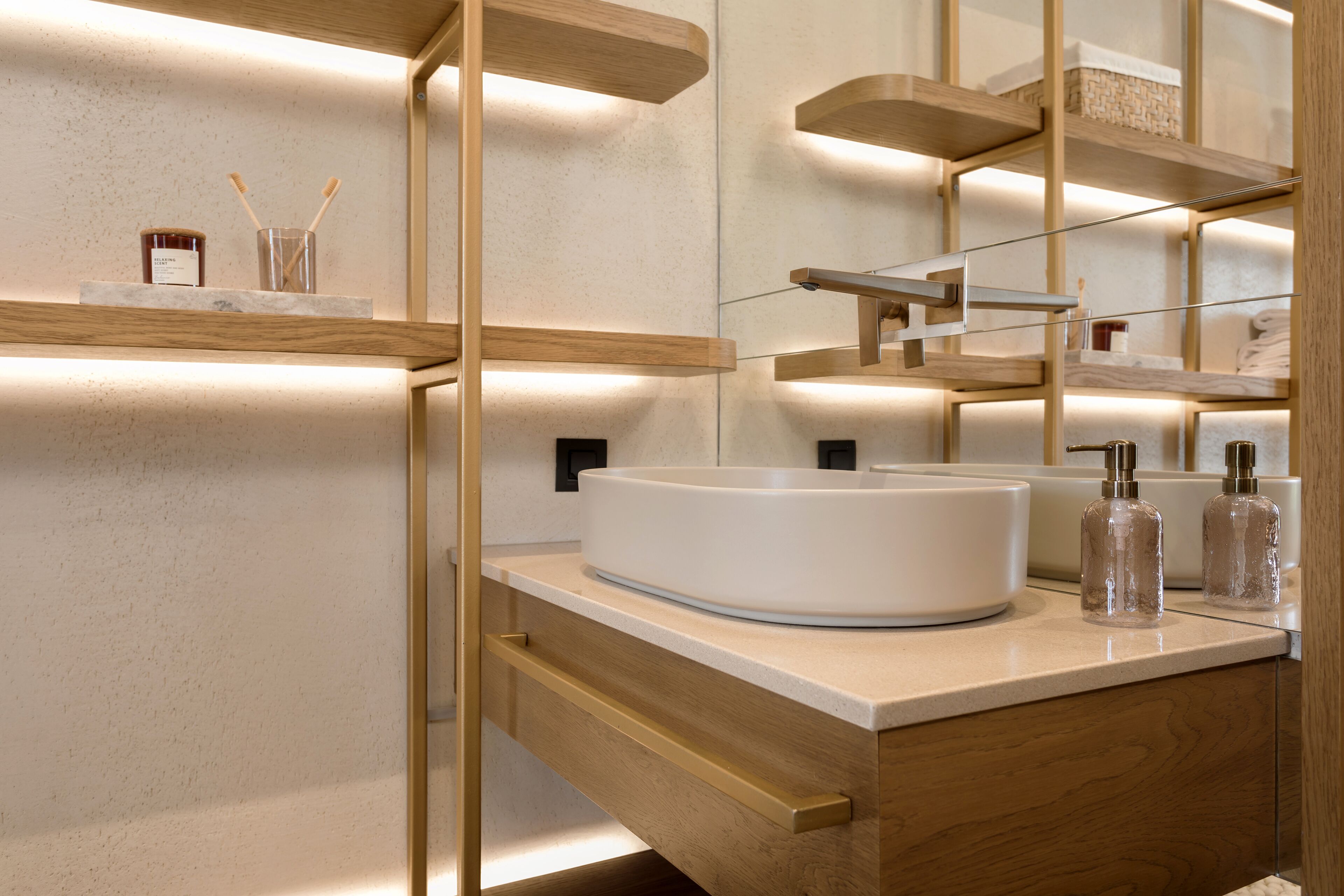 Un baño moderno con un lavamanos redondo, repisas de madera y un espejo.