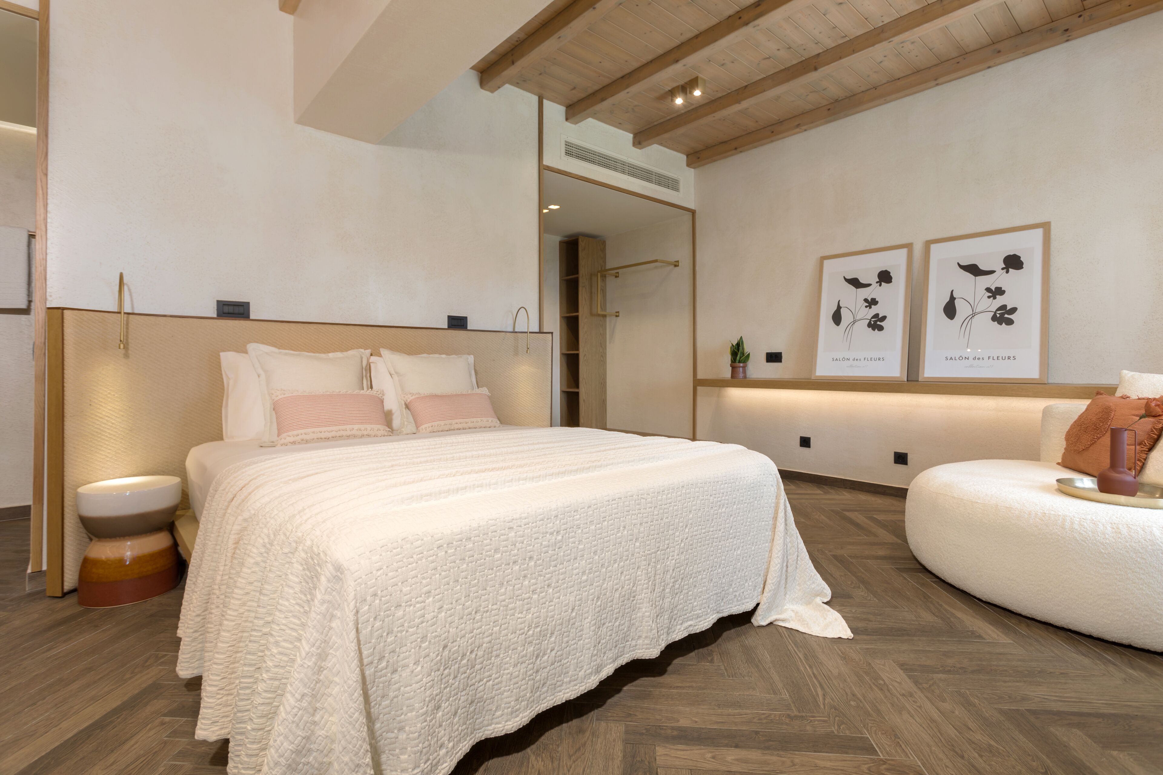 A modern bedroom with a large bed, a bedside table, a round seating area, and two framed floral artworks on the wall.