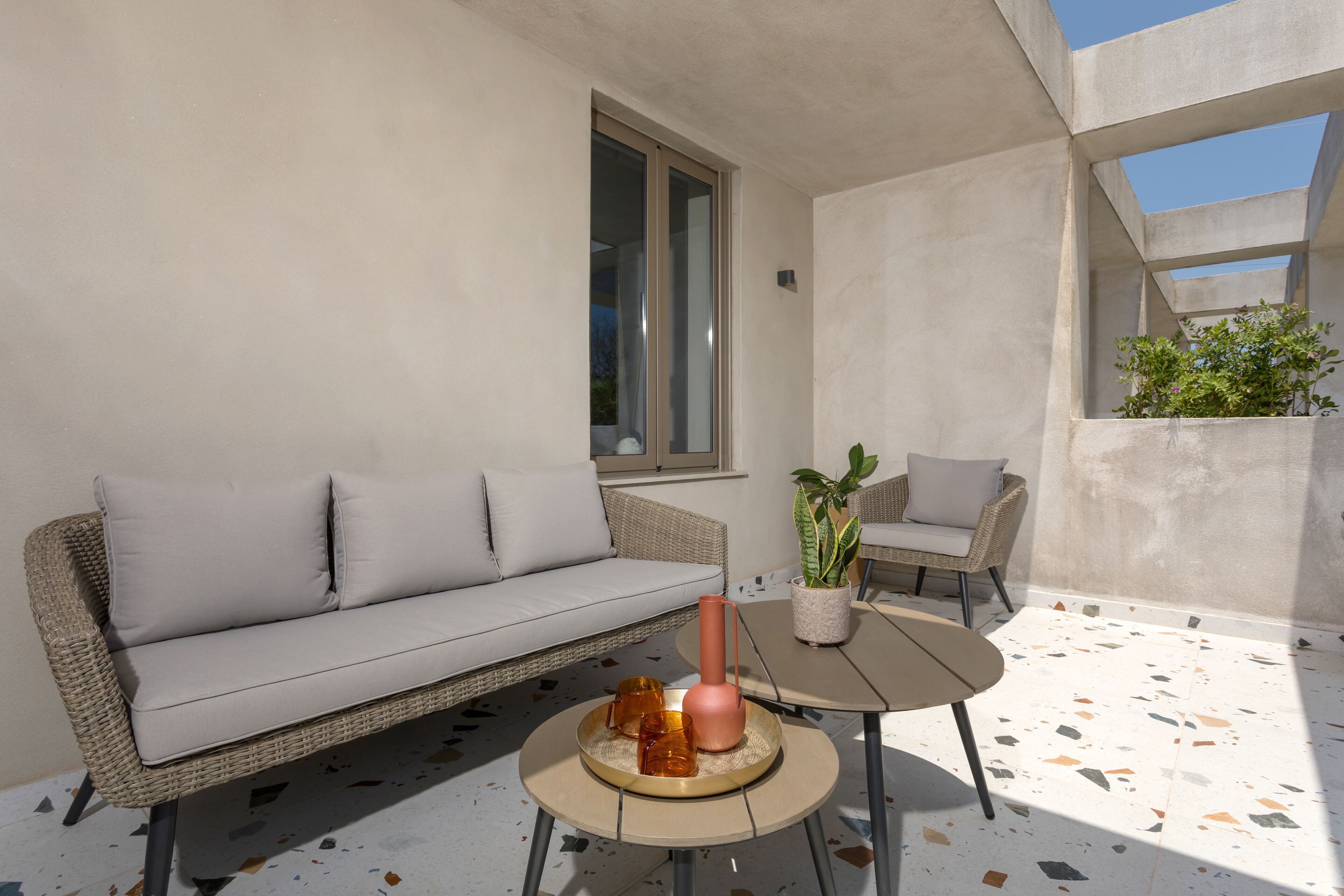 A modern outdoor seating area with a wicker sofa, a round table, and a potted plant.