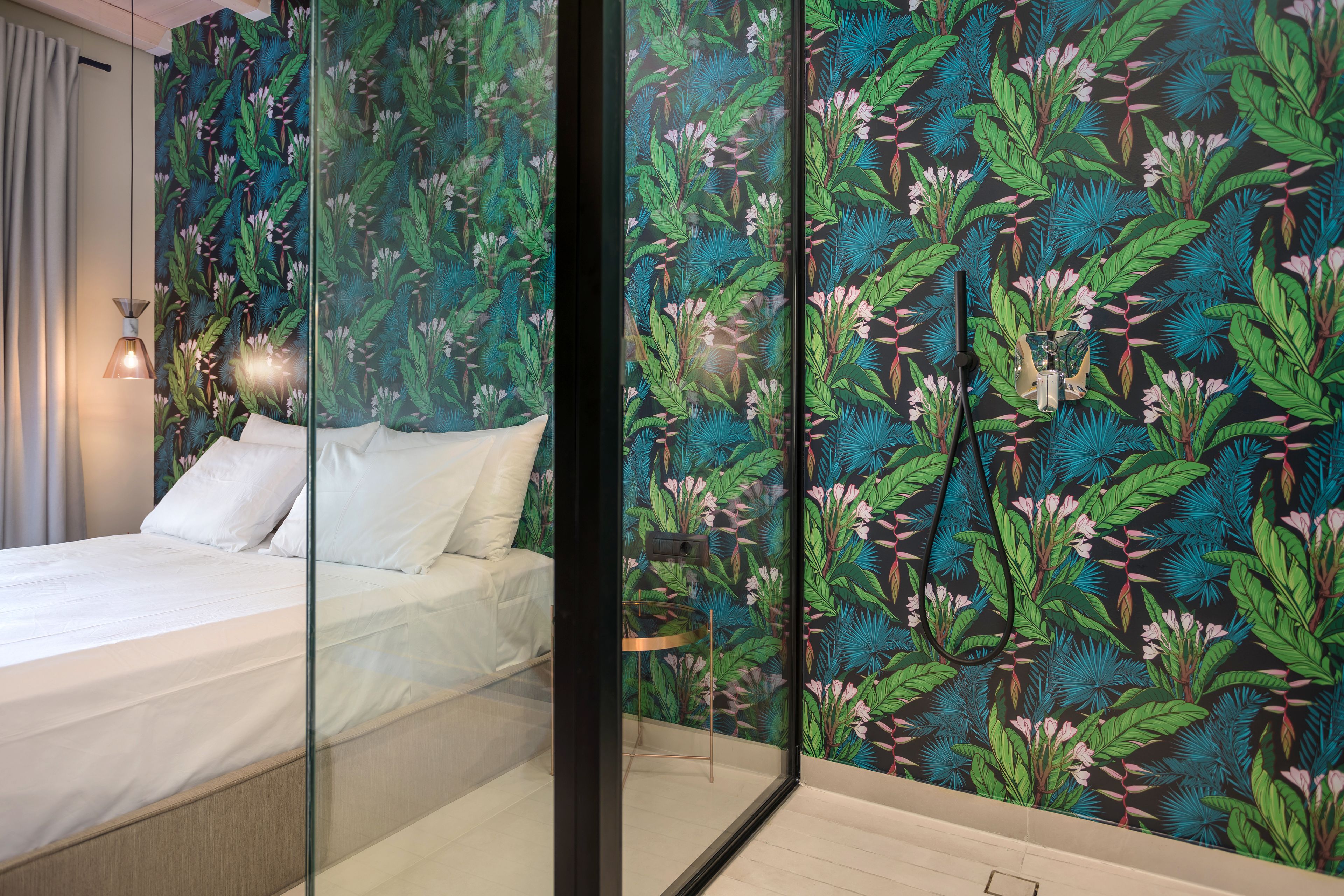 A bedroom with a bed, a glass partition, and a wall with a tropical leaf pattern.