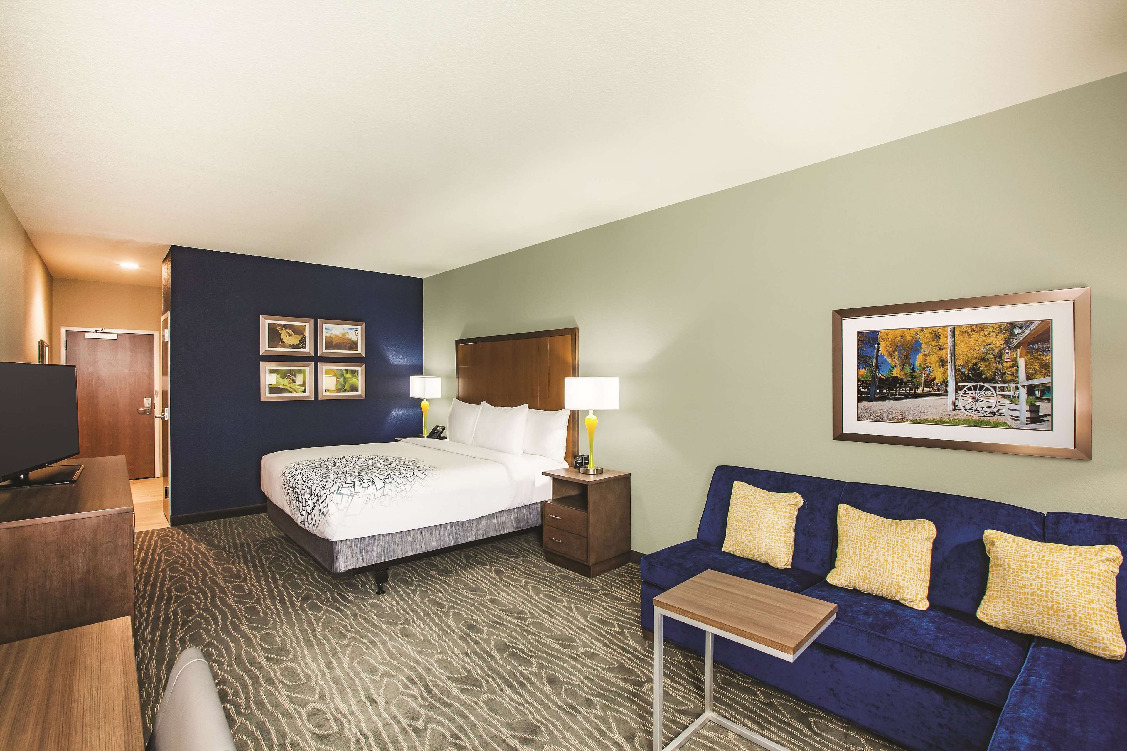 A hotel room with a bed, a desk, a sofa, and a framed picture on the wall.