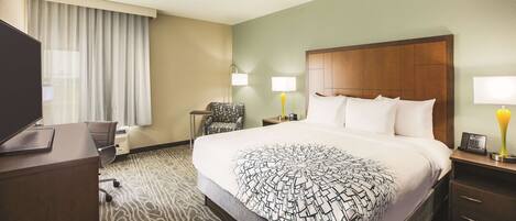 A hotel room with a large bed, a desk, a chair, two bedside lamps, and a television.