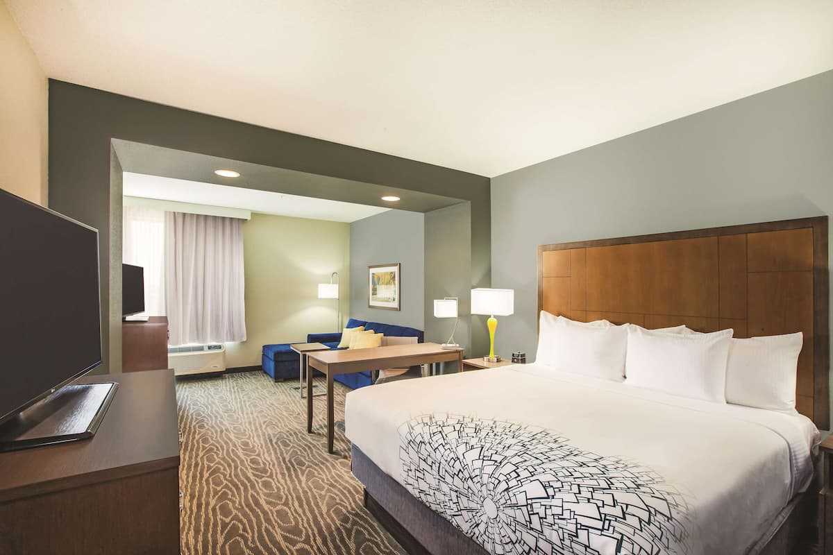 Ein Hotelzimmer mit einem großen Bett, einem Schreibtisch, einem Stuhl, einem Fernseher und einem Fenster mit Vorhängen.