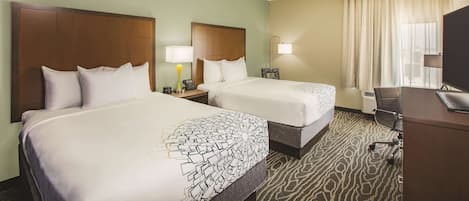 A hotel room with two beds, a desk, a chair, a TV, and a window with curtains.