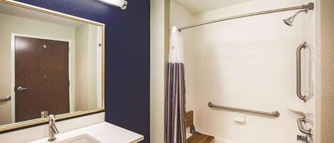 A bathroom with a white sink, a mirror, a shower with grab bars, and a door.