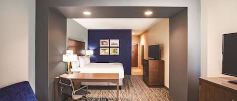 A hotel room with a bed, a desk with a lamp, a TV, and a blue sofa.