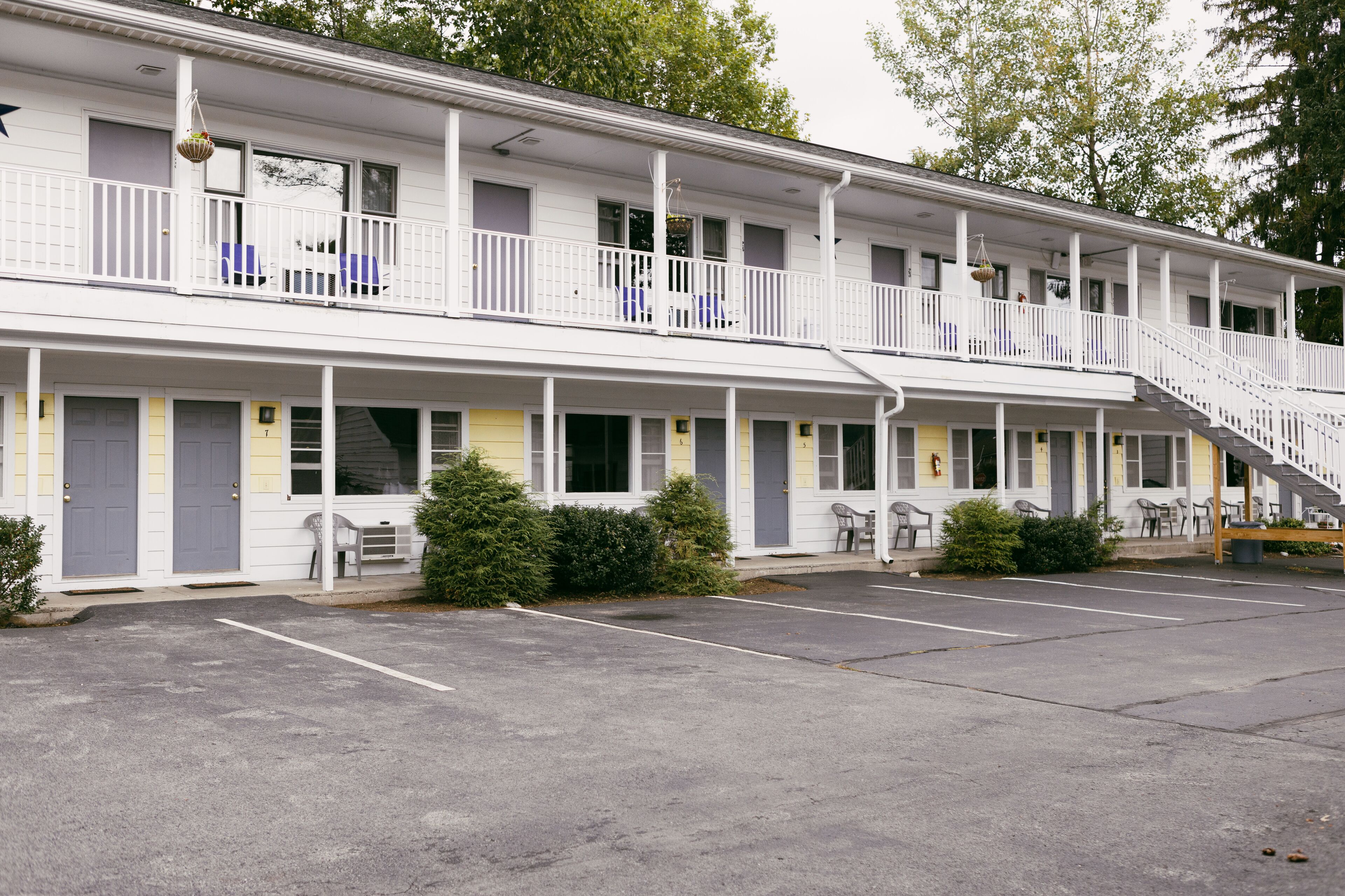 A motel with two-story balconies, a covered parking area, and a row of single-story rooms.