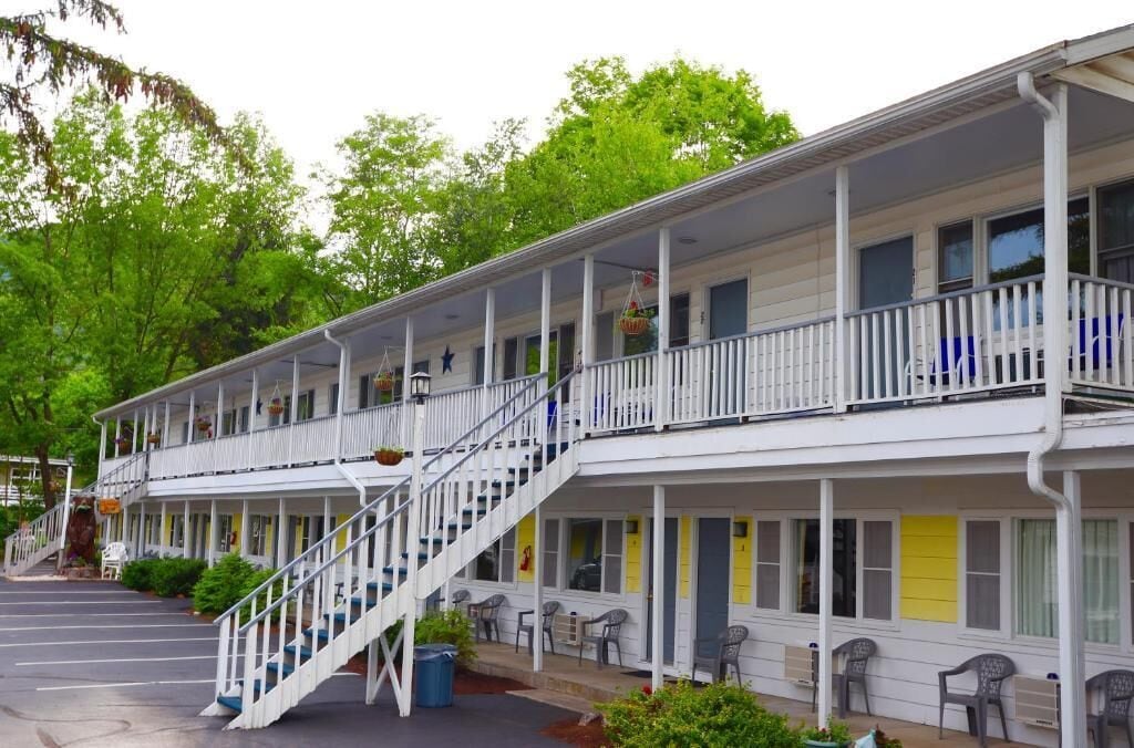 Un motel de dos pisos con un porche cubierto, mobiliario exterior y una escalera que conduce al nivel superior.