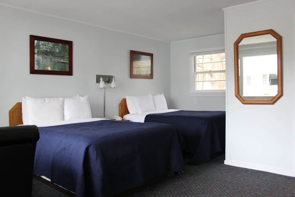 A hotel room with two beds, a large mirror, and two framed pictures on the wall.